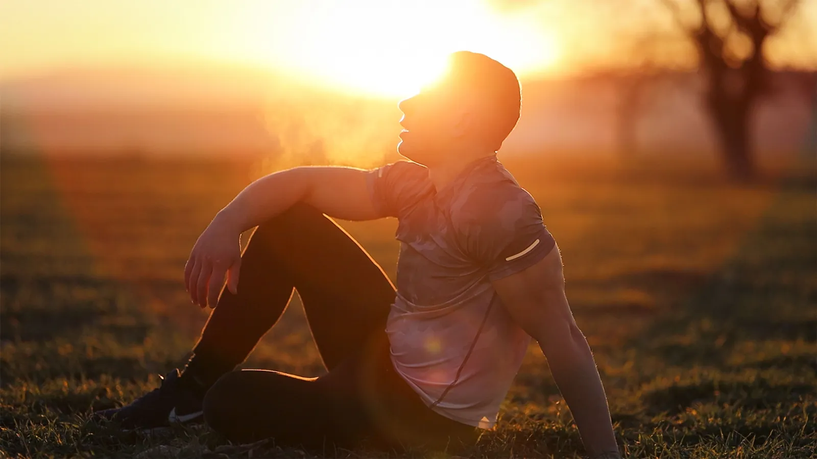 A man sitting outdoors at sunset, visible breath in the cold air