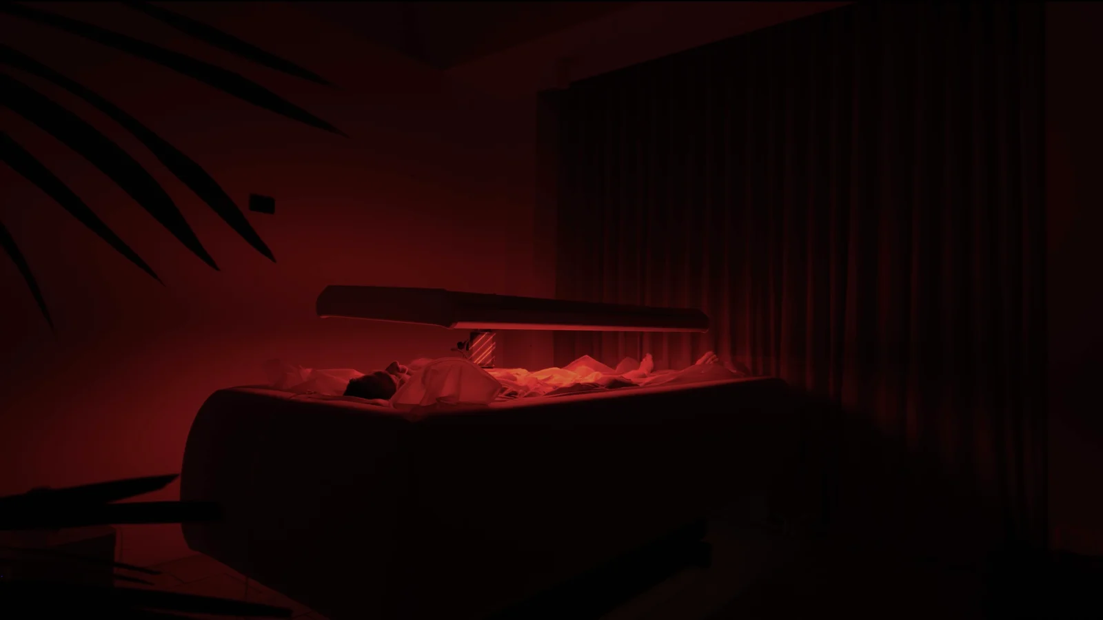 Side view of a red-light panel above a treatment bed in a softly lit room.