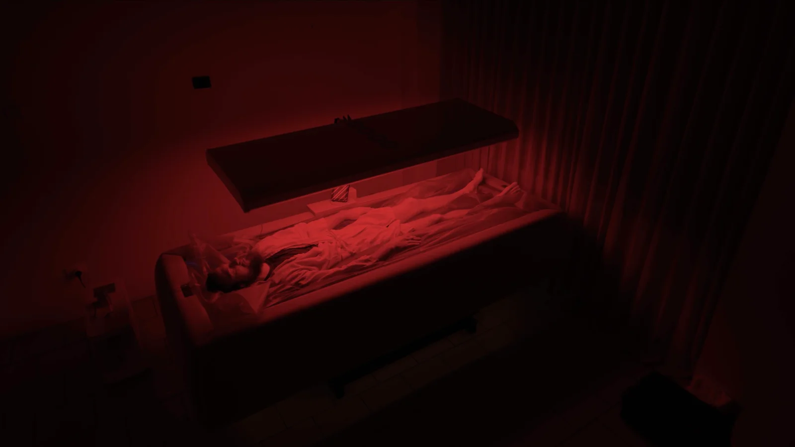 A person resting beneath an overhead red-light panel, viewed from above.